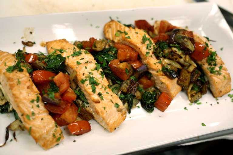 The stuffed salmon is plated and topped with the sautéed eggplant and tomato and garnished with fresh herbs.