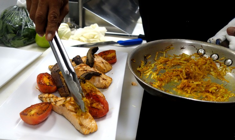 The grilled salmon being garnished with the sautéed leeks, portobello mushroom and roma tomato
